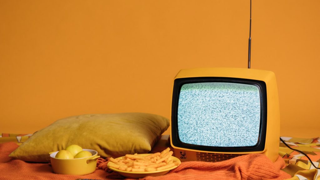Gammelt gult fjernsyn med sne på skærmen ved siden af en pude og en skål snacks