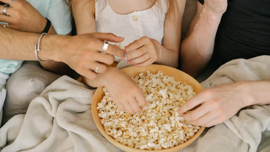 Hænder der tager popcorn fra en skål på et tæppe i sofaen